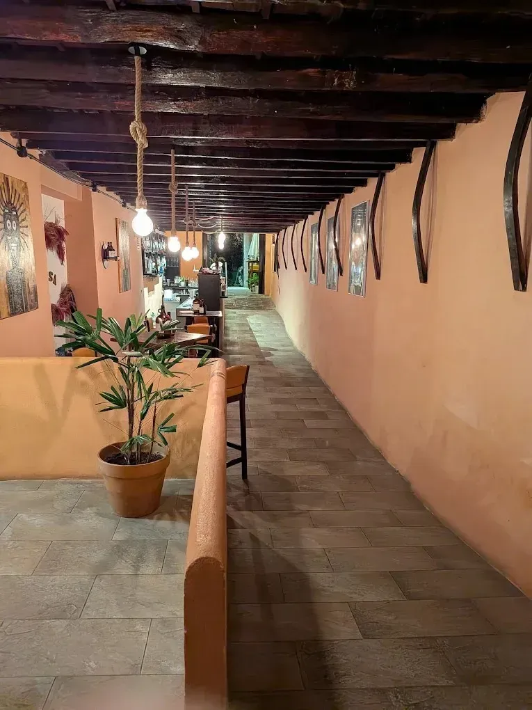 Interior largo y estrecho de un restaurante con paredes color durazno, techo de madera y una hilera de cuadros y luces.