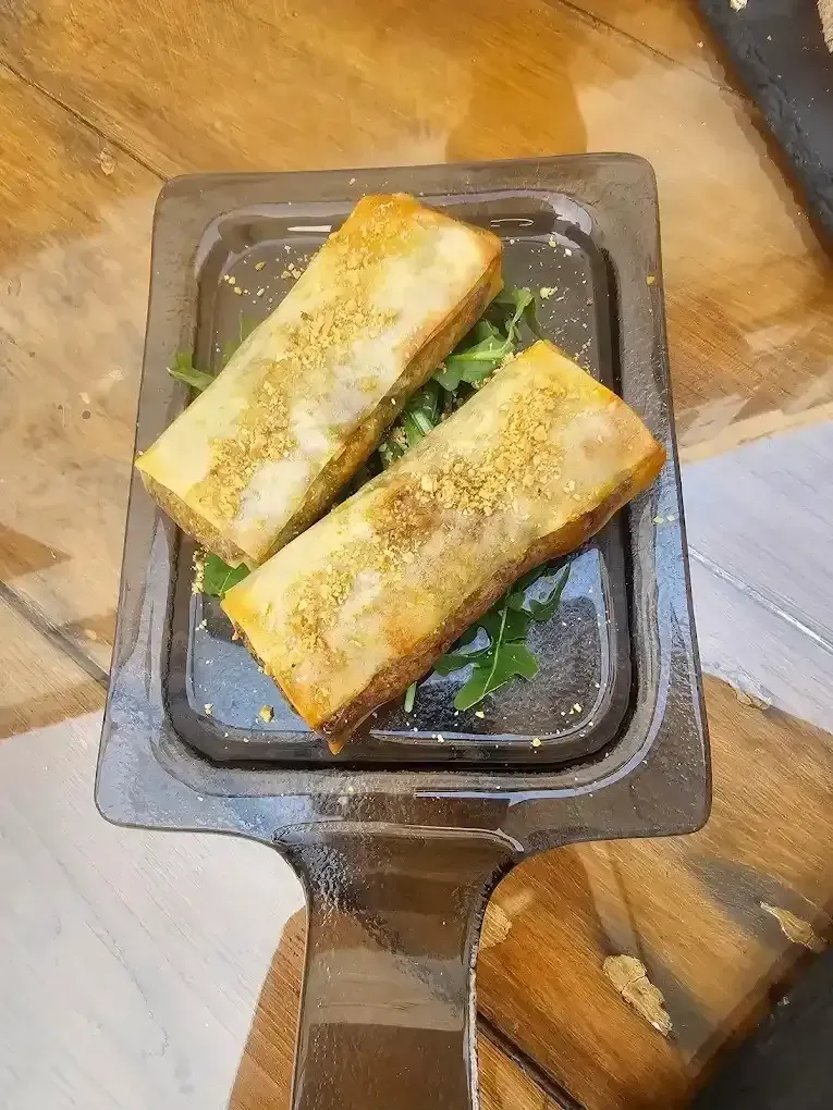 Dos rollitos de primavera de color marrón dorado en una bandeja oscura con guarnición verde, mesa de madera a la vista.