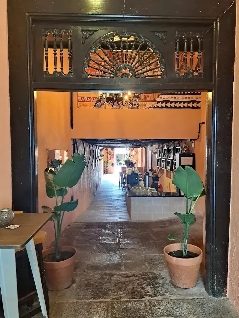 Una puerta abierta conduce a un callejón estrecho y bien iluminado, con plantas en macetas que flanquean la entrada.