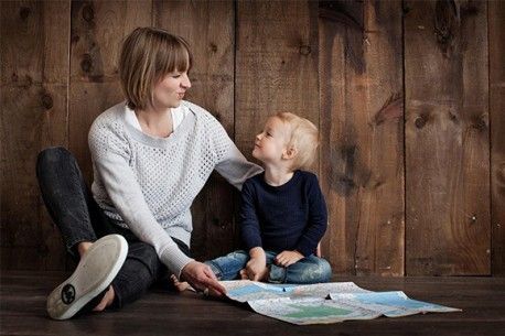 Mutter und Kind sitzen mit einer Landkarte auf einem braunen Boden und vor einer braunen Wand