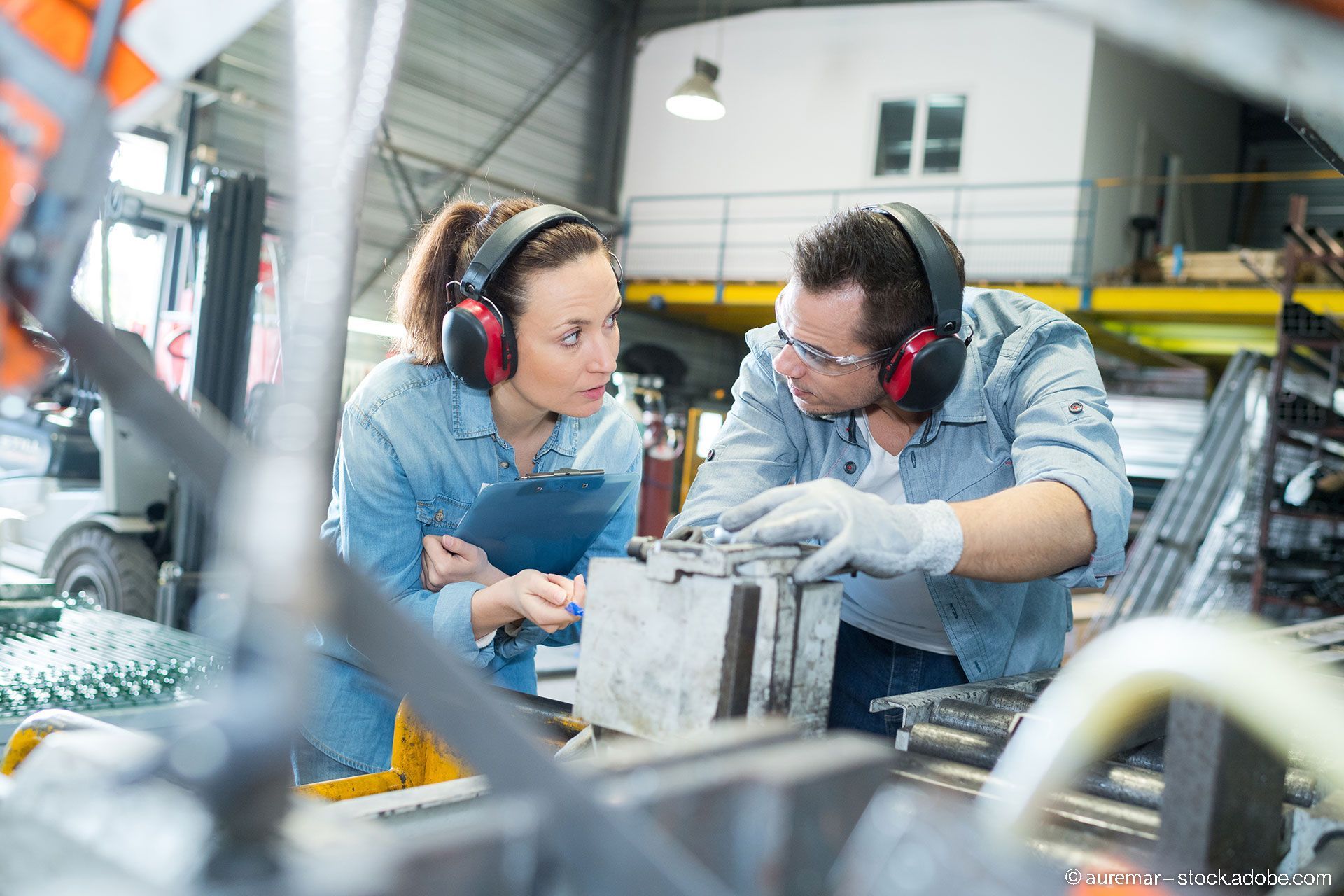 Zwei Personen arbeiten in einer Fabrik und tragen Gehörschutz, um ihre Ohren vor Lärm zu schützen.
