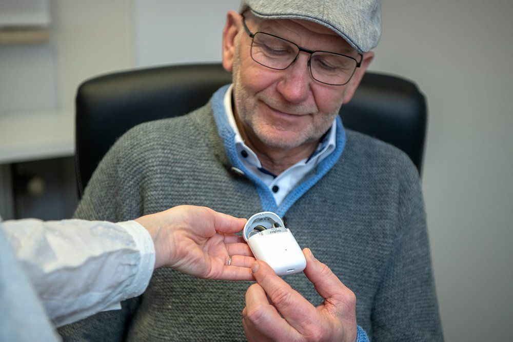 Ein Hörgeräteakustiker zeigt einem zufriedenen Patienten einen Gehörschutz