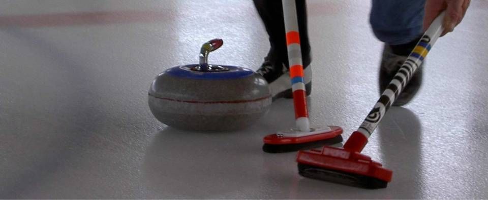 Pierre de curling sur une patinoire, deux joueurs balayant à côté.