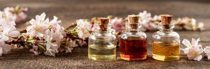 Flaschen mit ätherischen Ölen auf einer Holzoberfläche, umgeben von rosa und weißen Blumen.