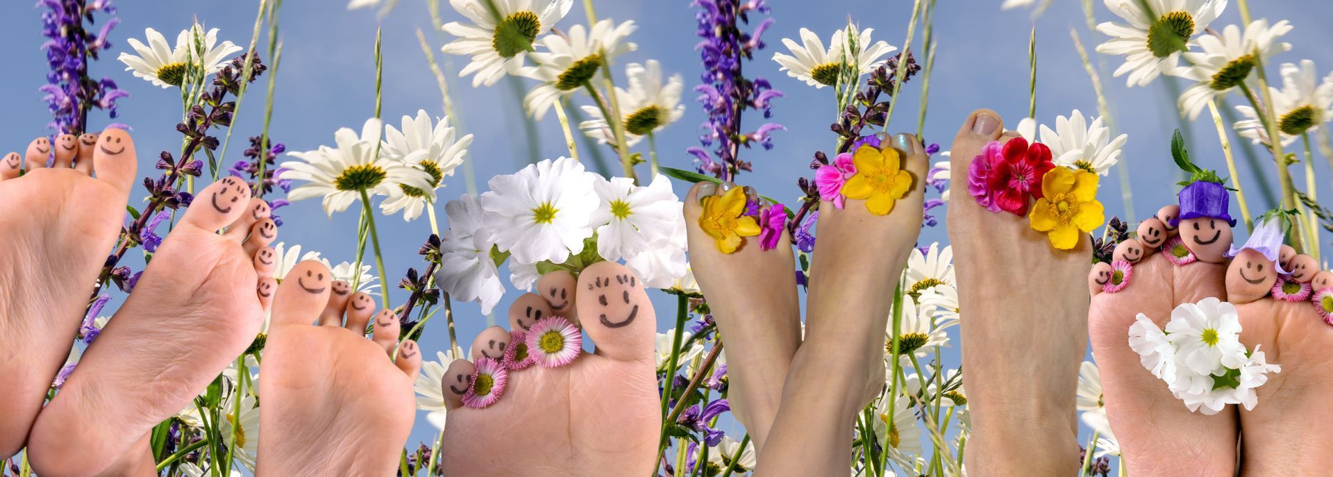 Mit Blumen geschmückte Füße und gezeichnete Gesichter inmitten eines Blumengartens.