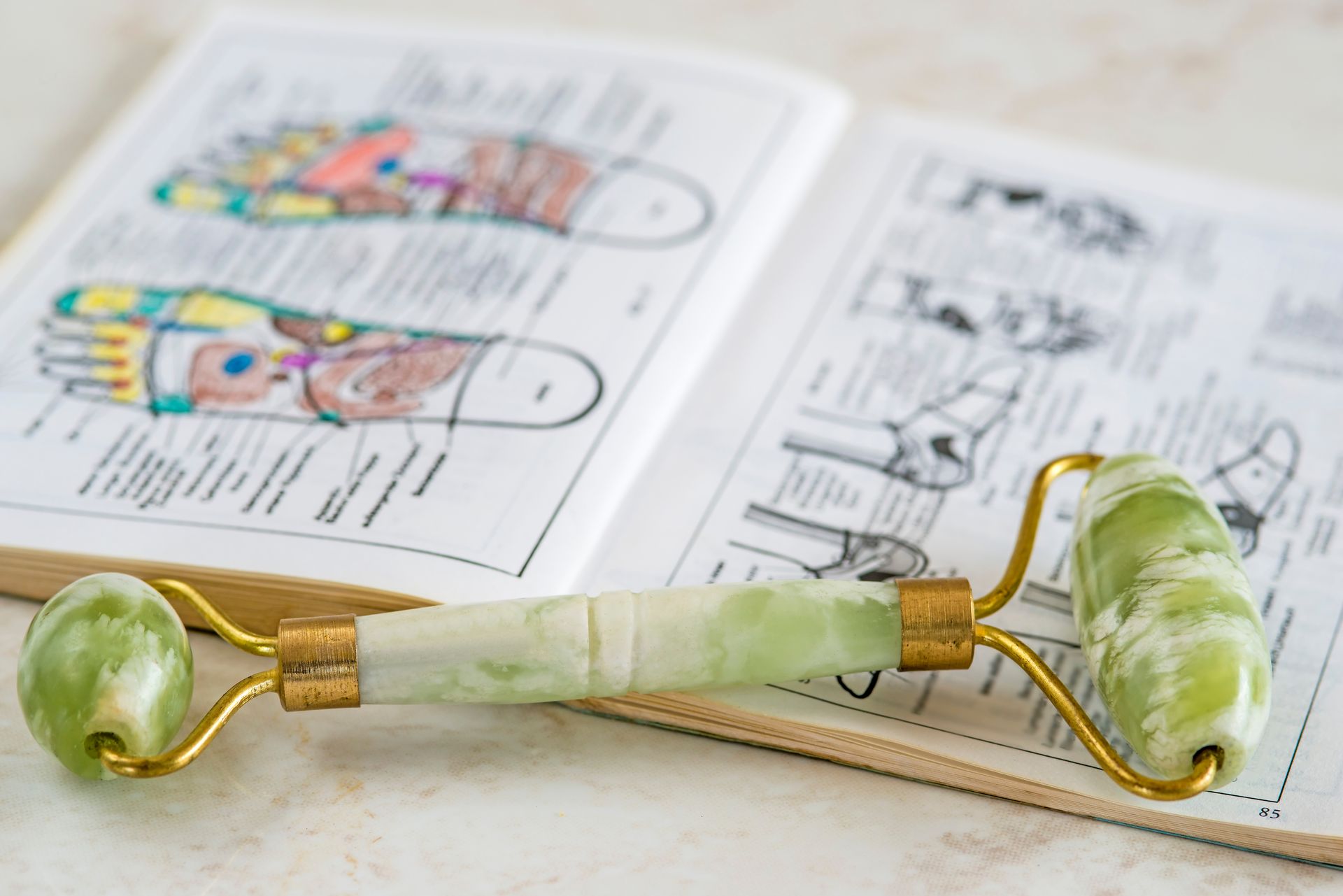 Jade-Gesichtsroller auf einem Buch mit Fußreflexzonenmassage-Diagrammen; goldene Beschläge, hellgrüner Stein.