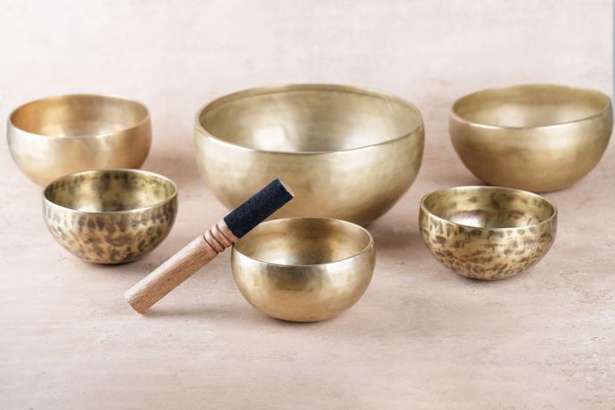 Goldene Klangschalen mit Schlägel auf hellrosa Untergrund.