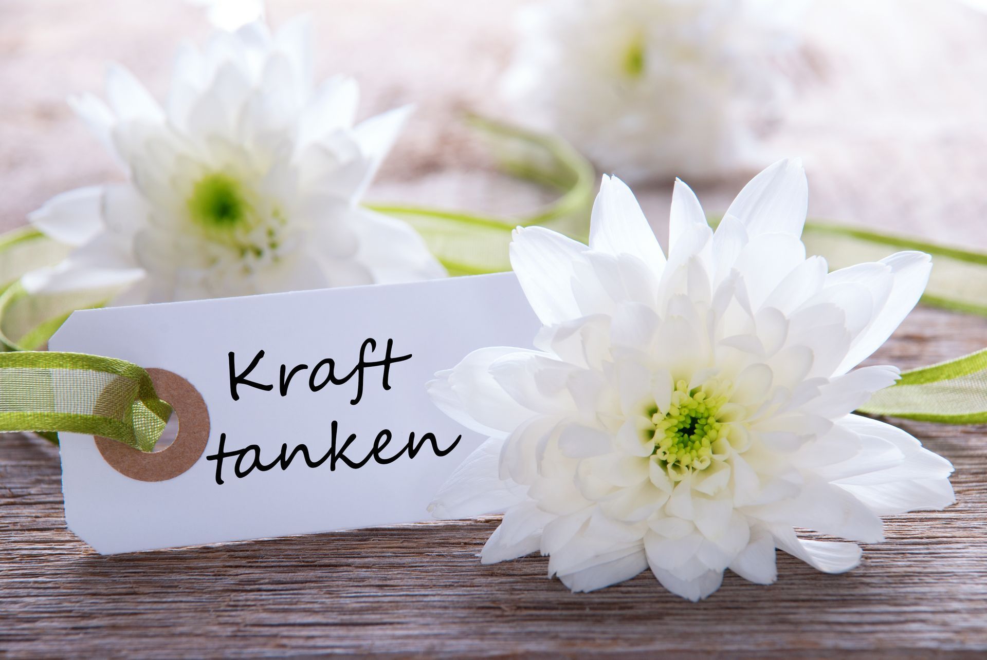 Weiße Blumen und ein Schild mit der Aufschrift „Kraft tanken“ auf einer Holzoberfläche.
