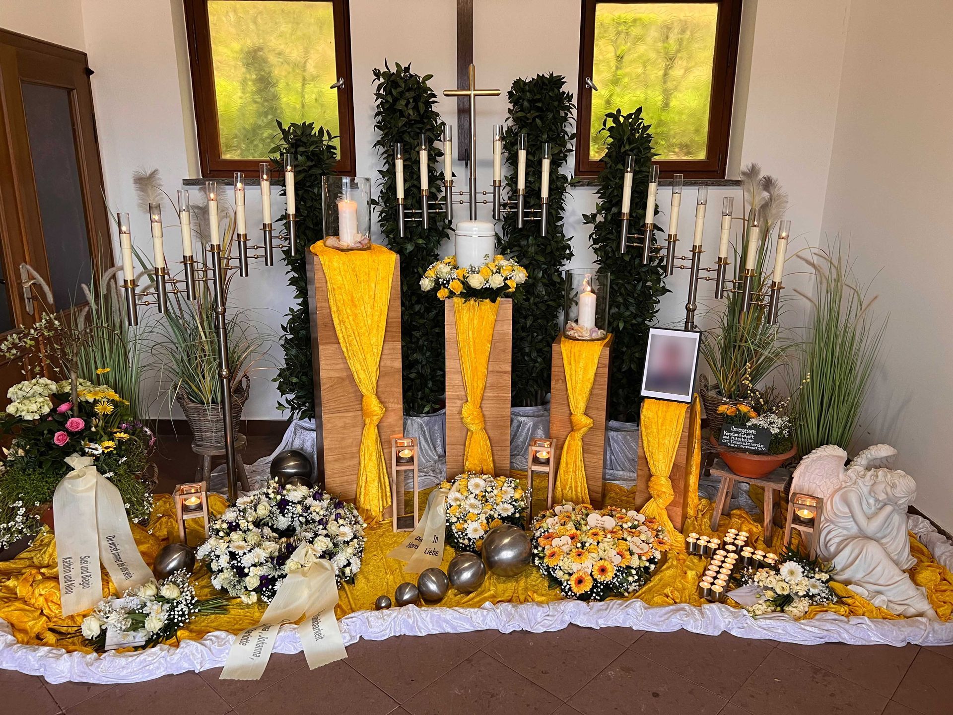 Grabgestaltung mit gelbem Blumenschmuck, Kerzen und Grablichtern in einer Kapelle