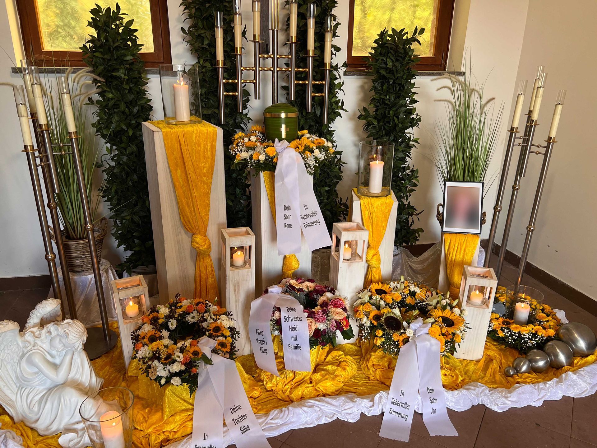 Grabgestaltung mit gelbem Blumenschmuck, Kerzen und Grablichtern bei einer Trauerfeier