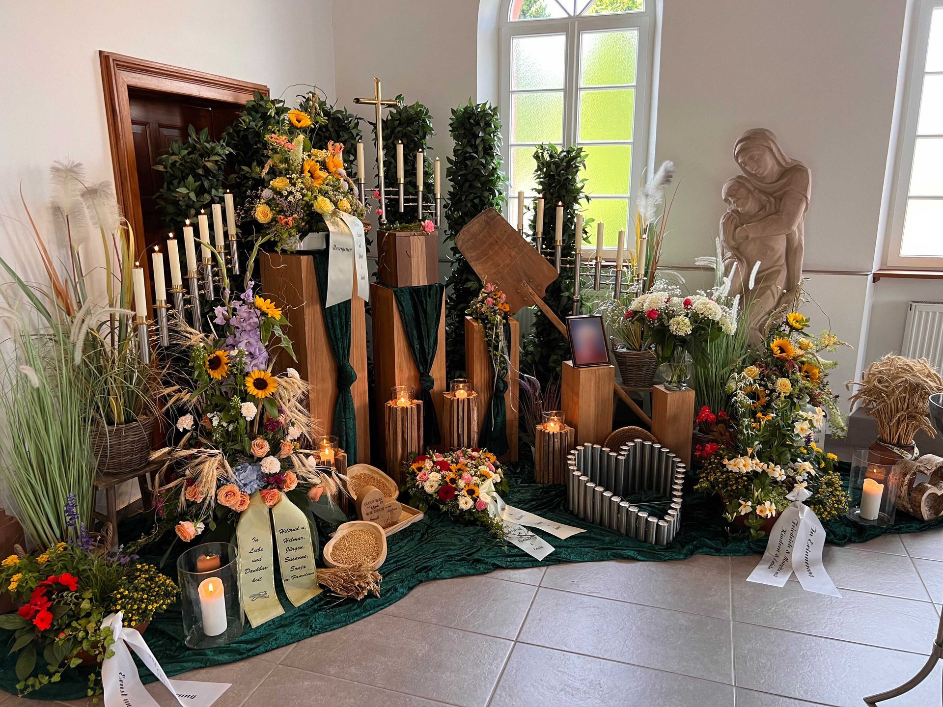 Grabgestaltung mit Sonnenblumen, Blumenschmuck, Grablichtern und Kerzen in einer Kapelle