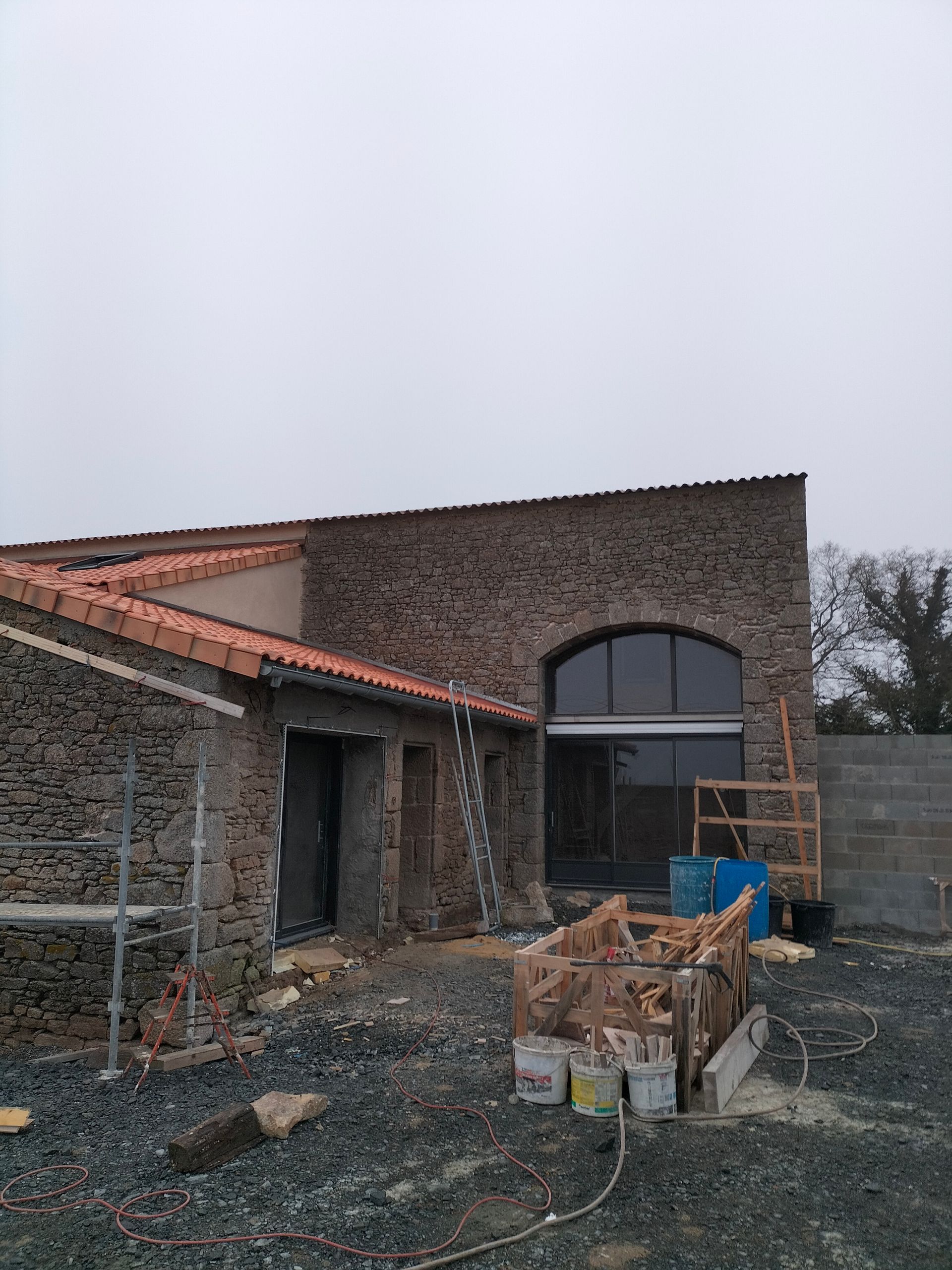 Maison en briques partiellement construite avec porte cintrée, matériaux de construction et gravier dans la cour avant
