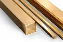 Três barras quadradas de latão estão sobrepostas umas às outras sobre uma superfície branca.