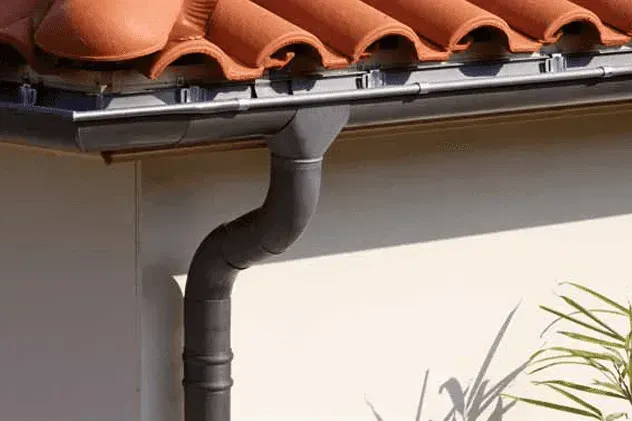 Uma calha na lateral de uma casa com telhado de telhas.