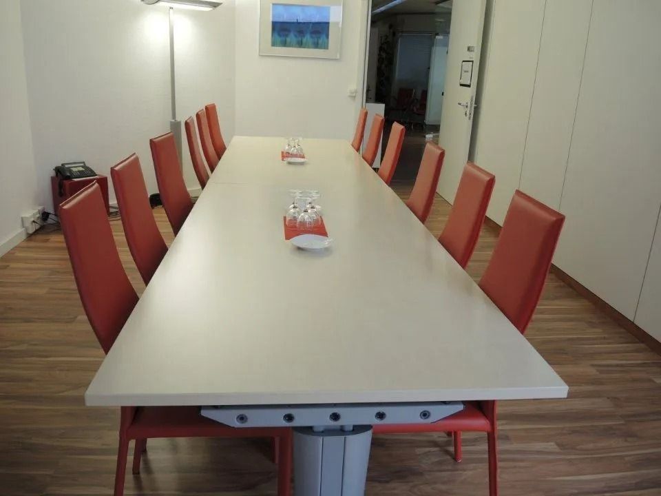 Langer weisser Konferenztisch mit roten Stühlen in einem minimalistischen Besprechungsraum