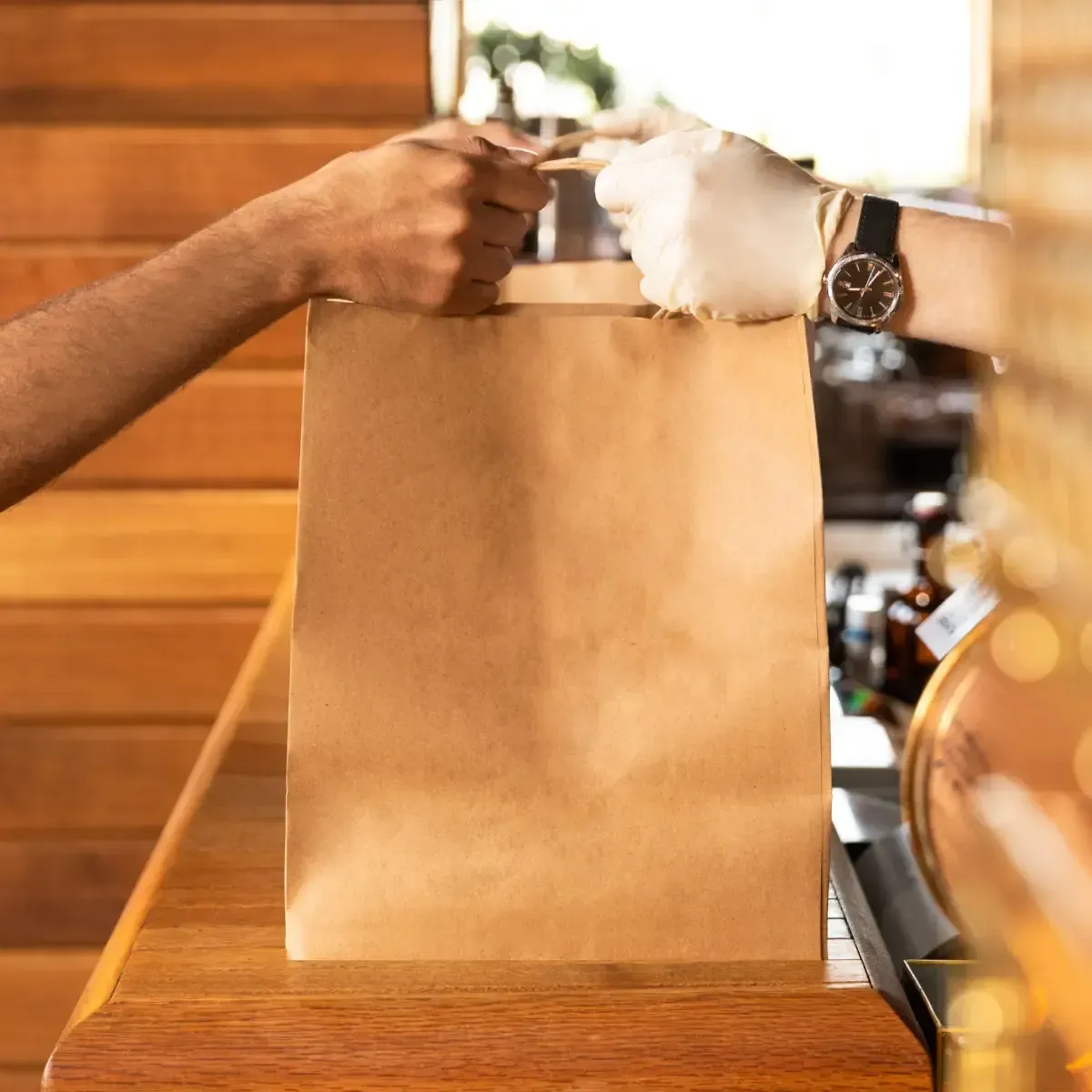 Una persona con guantes blancos le entrega una bolsa de papel a otra persona por encima de un mostrador de madera.