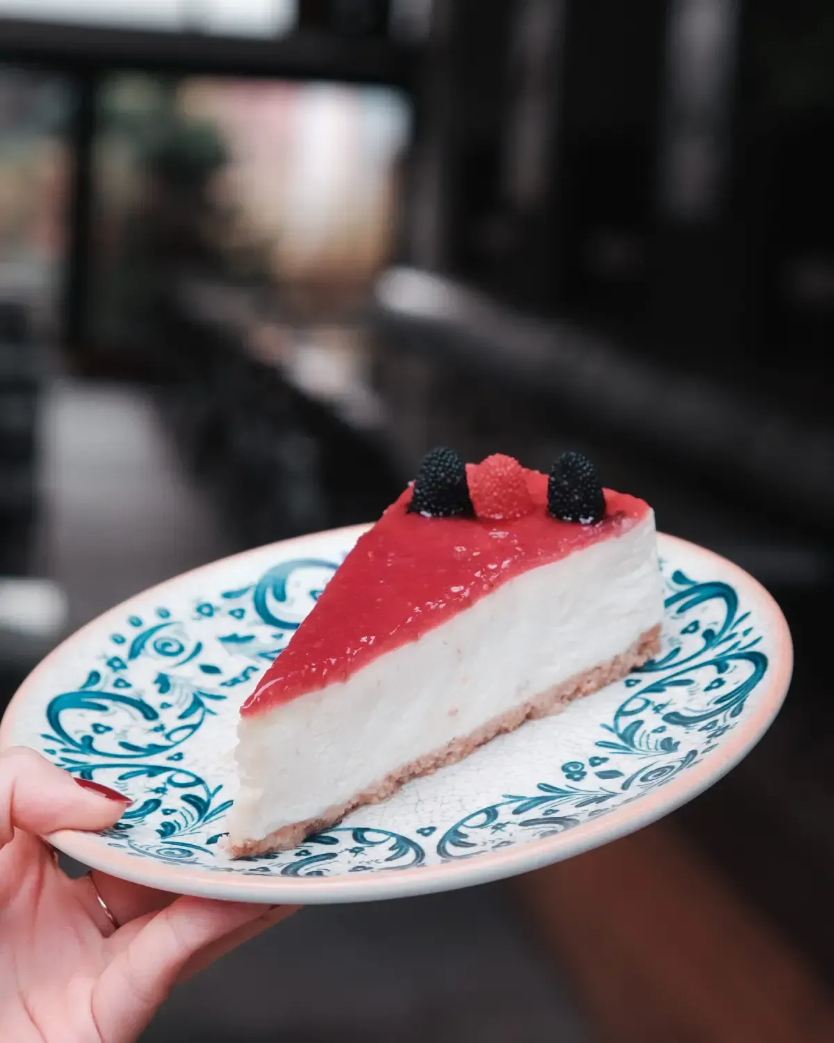 Una porción de tarta de queso con cobertura de frutos rojos y dos moras, servida en un plato