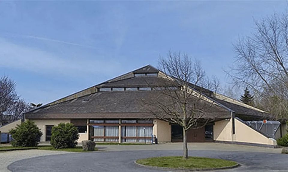 Un grand bâtiment avec un toit en forme de triangle et un arbre devant lui.