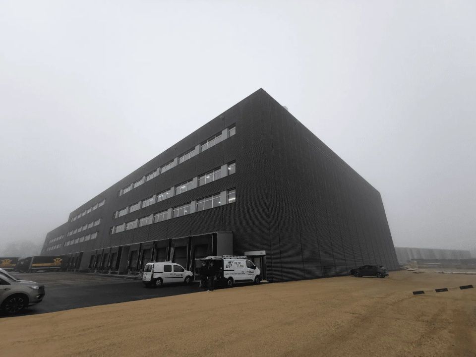 Un grand bâtiment avec beaucoup de voitures garées devant lui par une journée brumeuse.