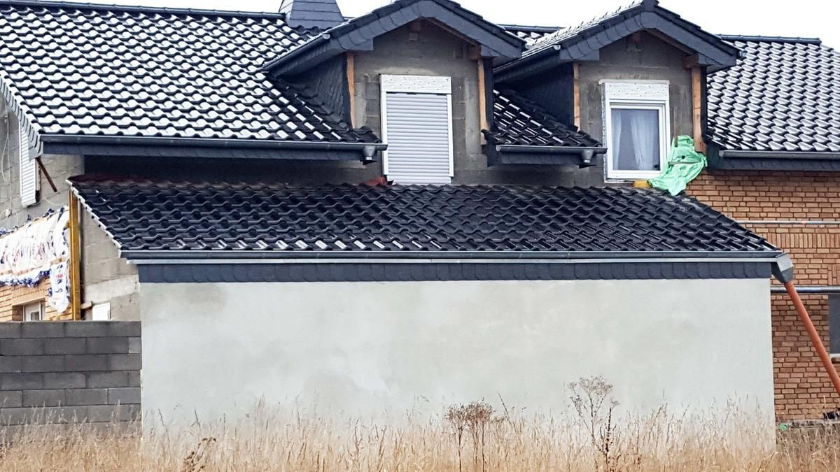 Auf einem Feld wird ein Haus mit einem schwarzen Ziegeldach gebaut.