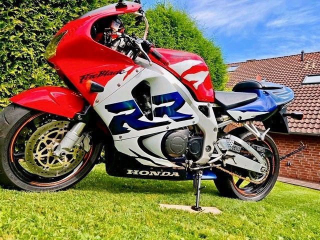 Rot-weiß-blaues Honda CBR900RR-Motorrad auf Gras geparkt.