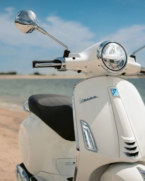 Weißer Vespa-Roller an einem Strand mit Meer im Hintergrund.