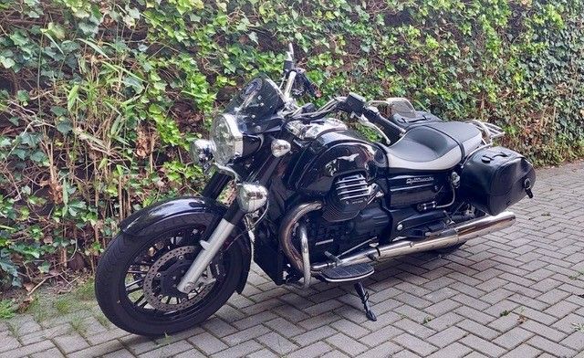 Schwarzes Motorrad, das auf einer Ziegelfläche vor einer grünen Wand geparkt ist.