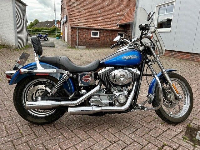 Blaues Harley-Davidson-Motorrad mit schwarzem Sitz und Rückenlehne auf einer gemauerten Fläche geparkt.
