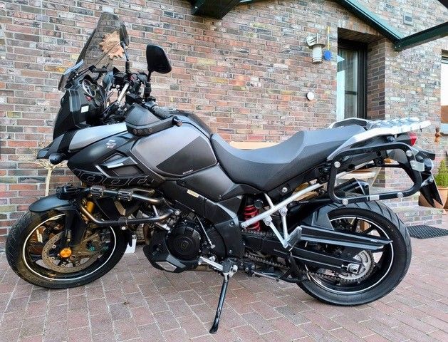 Schwarzes Motorrad mit zusätzlichen Schutzbügeln, auf einer gemauerten Terrasse geparkt.