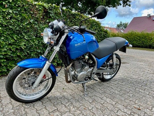 Blaues Sachs Roadster-Motorrad, geparkt auf einer gepflasterten Auffahrt neben einem grünen Busch.