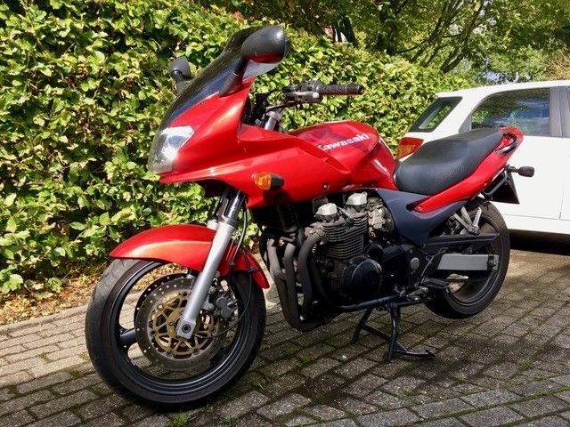 Ein rotes Motorrad ist neben einem weißen Auto geparkt