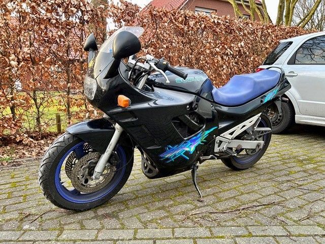 Ein schwarz-blaues Motorrad ist neben einem silbernen Auto geparkt.