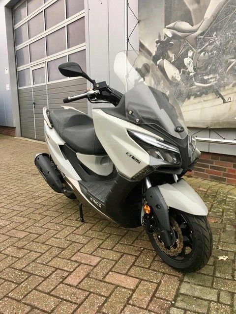 Ein weißer Motorroller ist auf einem gepflasterten Gehweg vor einem Gebäude geparkt.