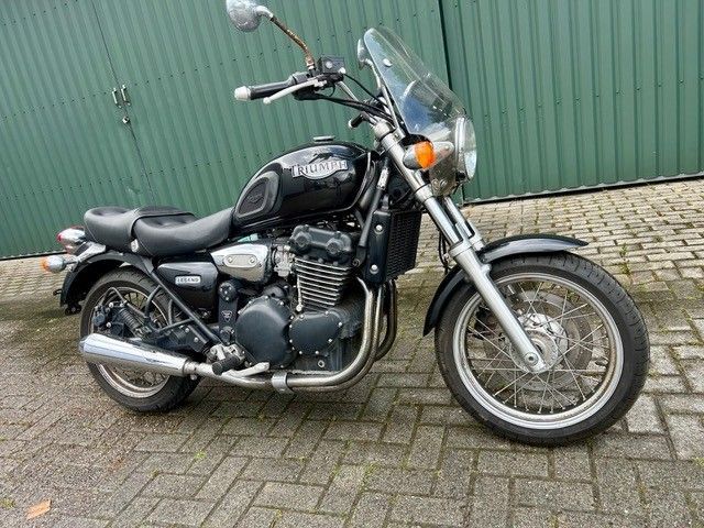 Ein schwarzes Cruiser-Motorrad parkt auf Pflastersteinen vor einer grünen Wellblechwand.