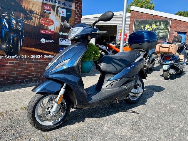 Ein blauer Motorroller ist vor einem Backsteingebäude geparkt.