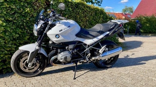 Weißes BMW-Motorrad, geparkt vor einer grünen Hecke, an einem sonnigen Tag.
