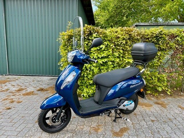 Ein blauer Motorroller parkt vor einem grünen Gebäude.