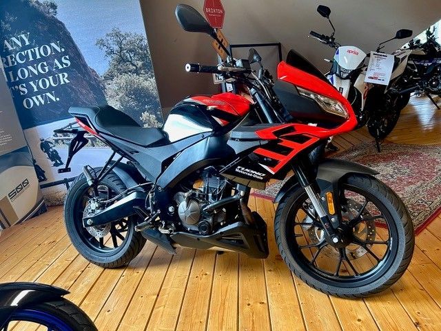 Ein rot-schwarzes Sportmotorrad auf einem Holzboden, im Hintergrund weitere Motorräder.