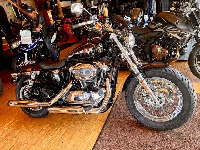 Ein schwarzes Cruiser-Motorrad steht in einem Innenraum zwischen anderen Motorrädern auf einem Holzboden.