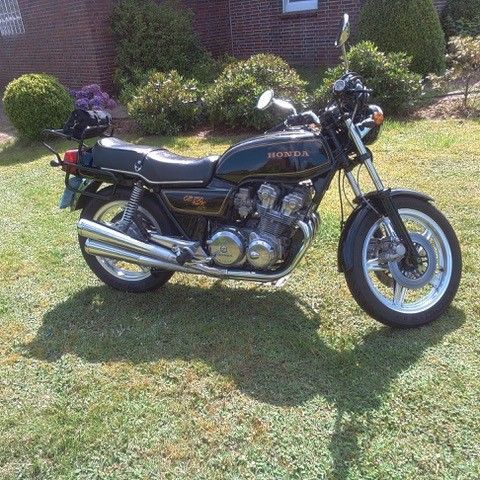 Ein schwarzes Motorrad ist im Gras vor einem Backsteingebäude geparkt.