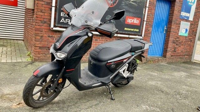 Ein schwarzer Motorroller ist vor einem Backsteingebäude geparkt.