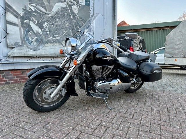 Ein schwarzes Motorrad ist auf einem gepflasterten Gehweg vor einem Gebäude geparkt.