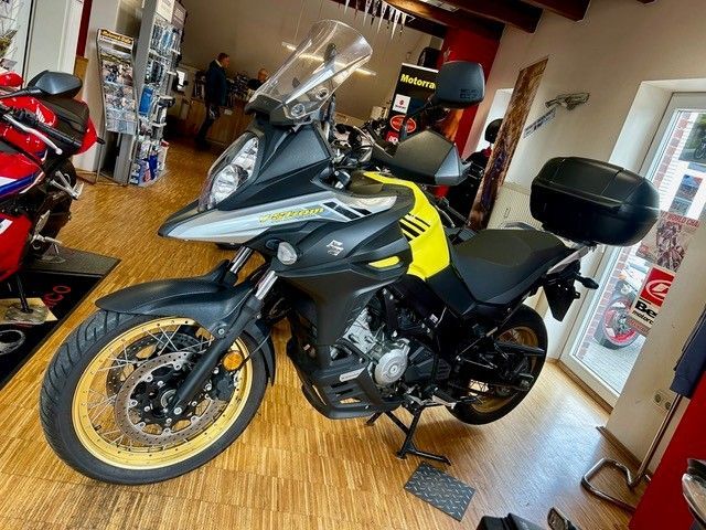 Schwarzes und graues Tourenmotorrad mit gelben Felgen, das in einer Halle auf einem Holzboden geparkt ist.
