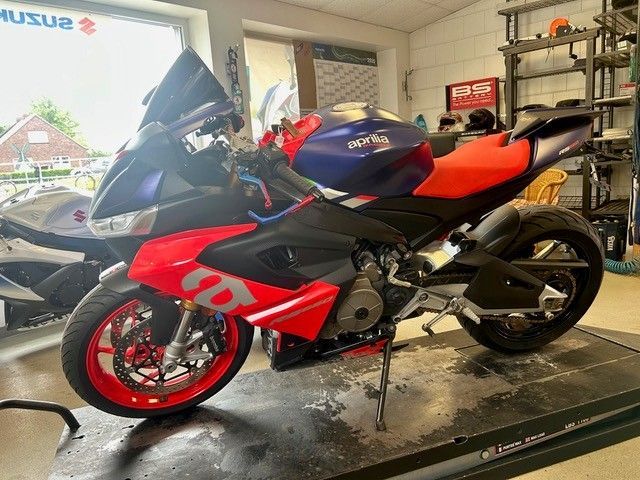 Ein rot-schwarzes Sportmotorrad mit roten Felgen steht in einem Ausstellungsraum; dahinter steht ein weiteres Motorrad.