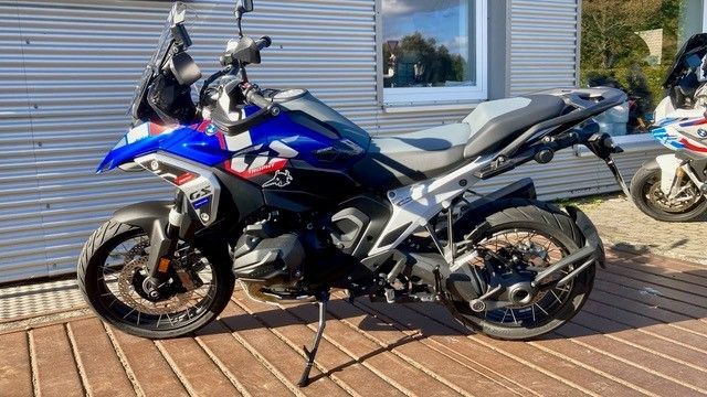 Ein blaues Motorrad ist auf einem gepflasterten Gehweg vor einem Gebäude geparkt.