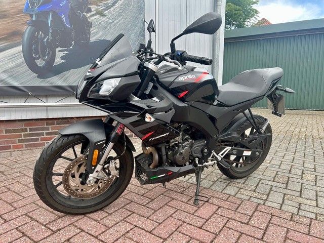Ein schwarzes Sportmotorrad parkt auf dem Backsteinpflaster neben einem Gebäude mit einem Motorradplakat.