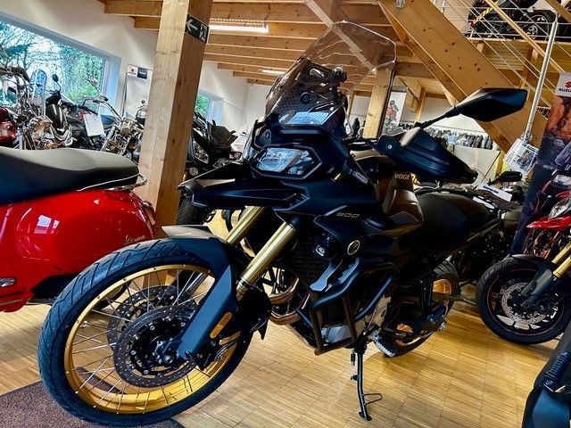 In einem Ausstellungsraum parkt ein Motorrad neben einem roten Motorroller.