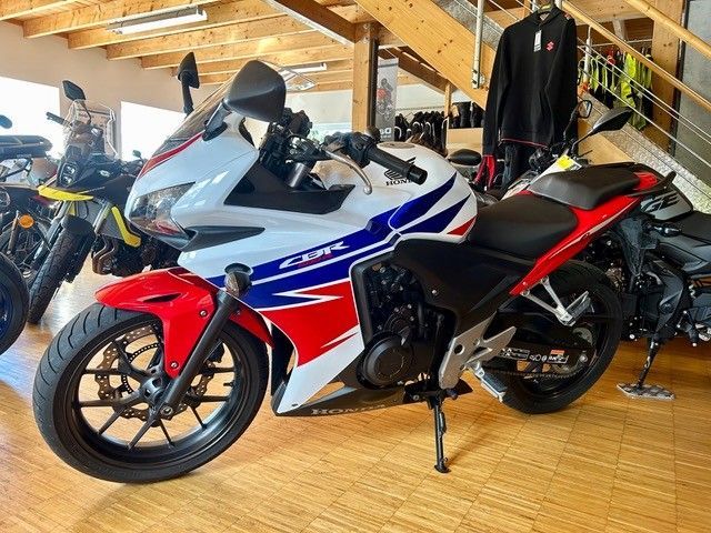 Ein rot-weiß-blaues Honda-Sportmotorrad steht in einem Ausstellungsraum neben einem schwarzen Motorrad.