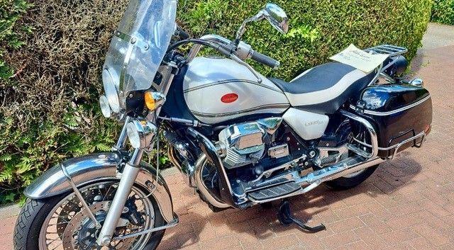 Silbernes und schwarzes Moto Guzzi California-Motorrad mit Windschutzscheibe und Satteltaschen, im Freien geparkt.