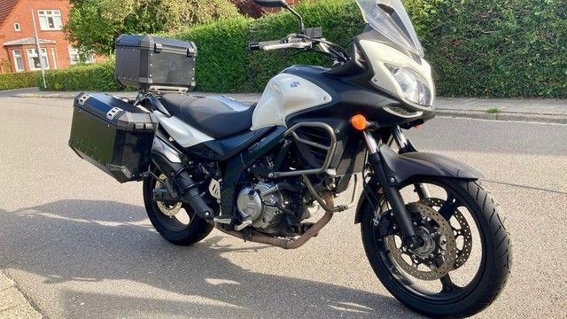 Schwarz-silbernes Suzuki V-Strom-Motorrad mit Seiten- und Topcase, das auf einer Straße geparkt ist.